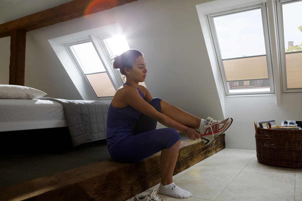 woman in gymwear putting trainers on in front of skylight windows fitted with velux blackout energy pleated blinds
