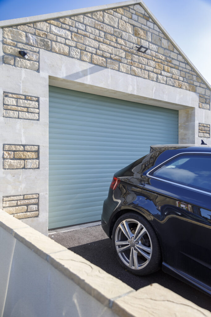 light blue SWS UK garage door on a building with a brick exterior and a black car parked in front